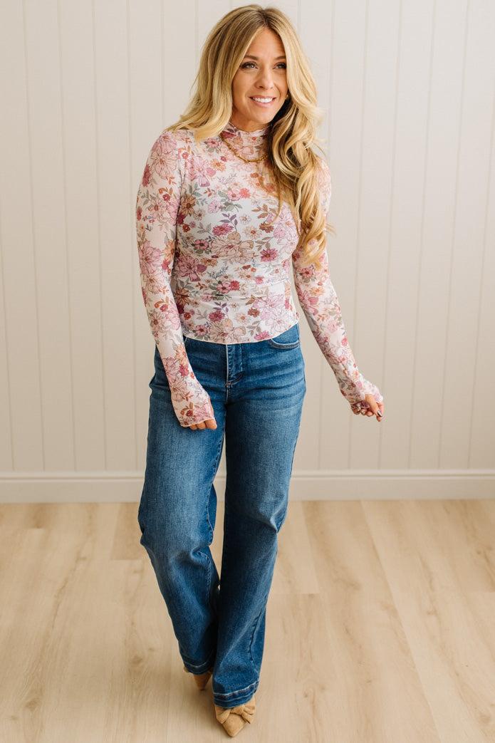 Woman wearing a floral long-sleeve top and blue jeans indoors.