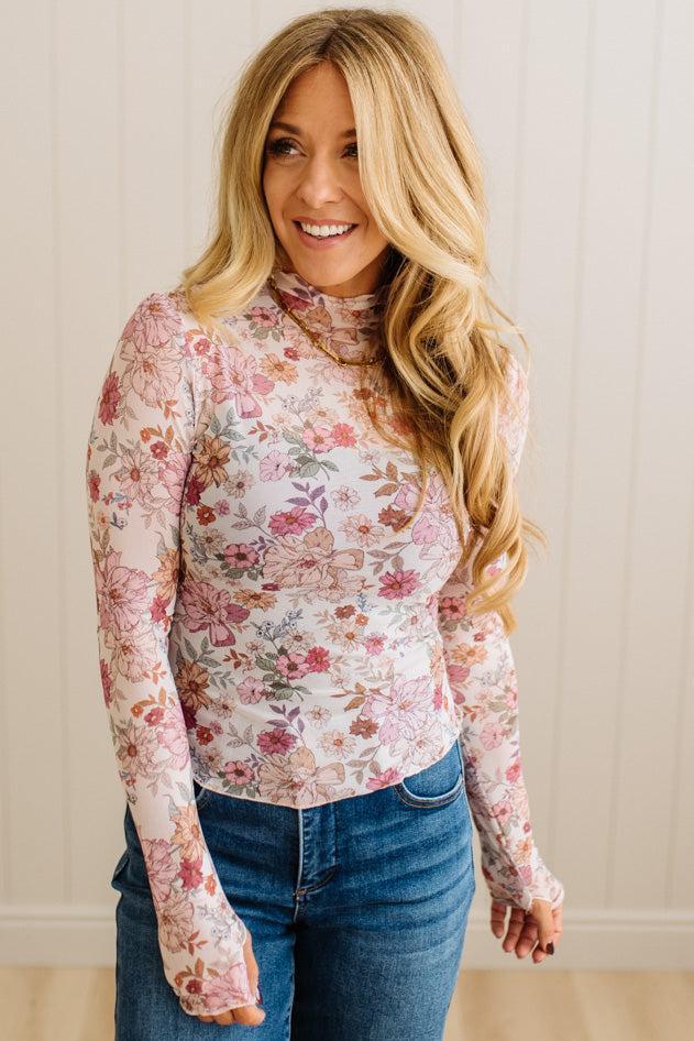 Woman wearing a floral long-sleeve top and blue jeans against a neutral background