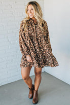 Woman wearing a floral dress with long sleeves against a white brick wall.