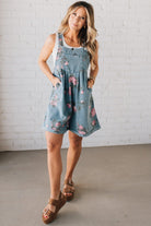 BLONDE WOMAN WEARING FLOWER PRINT WASHED DENIM WIDE LEG SHORTALLS WITH ADJUSTABLE BUTTONED SHOULDER STRAP