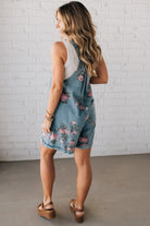 BLONDE WOMAN WEARING FLOWER PRINT WASHED DENIM WIDE LEG SHORTALLS WITH ADJUSTABLE BUTTONED SHOULDER STRAP