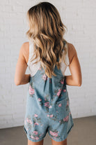 BLONDE WOMAN WEARING FLOWER PRINT WASHED DENIM WIDE LEG SHORTALLS WITH ADJUSTABLE BUTTONED SHOULDER STRAP