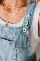 BLONDE WOMAN WEARING FLOWER PRINT WASHED DENIM WIDE LEG SHORTALLS WITH ADJUSTABLE BUTTONED SHOULDER STRAP