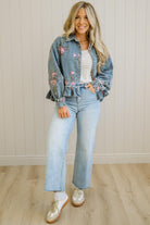 Woman wearing a floral embroidered denim jacket with light blue jeans indoors.