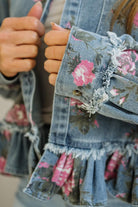 Close-up of a denim jacket with floral patterns and ruffled details.