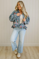 Woman wearing a floral denim jacket, white top, and light blue jeans against a neutral background