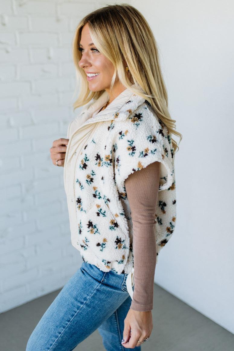 Woman wearing a floral blouse and jeans against a white brick wall.