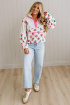 Woman wearing a floral blouse and jeans standing against a light wooden paneled wall.