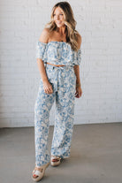 Blonde woman wearing a blue and white floral off the shoulder crop top with flowy overlay.