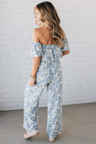 Blonde woman wearing a blue and white floral off the shoulder crop top with flowy overlay.