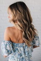 Blonde woman wearing a blue and white floral off the shoulder crop top with flowy overlay.