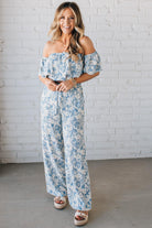 Blonde woman wearing a blue and white floral off the shoulder crop top with flowy overlay.