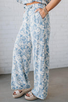 Blonde woman wearing blue and white floral wide leg pants with tie front and side pockets.