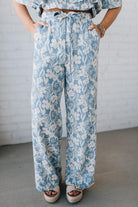 Blonde woman wearing blue and white floral wide leg pants with tie front and side pockets.