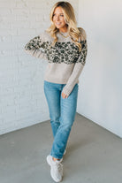 Woman wearing a gray sweater with leopard print sleeves and blue jeans against a white brick wall.
