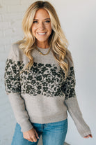 Woman wearing a gray sweater with black floral pattern and blue jeans against a white background