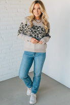 Woman wearing a patterned sweater and jeans against a white brick wall.