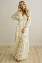 Woman wearing a long floral dress standing against a white paneled wall.