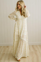 Woman wearing a long floral dress against a white paneled wall.
