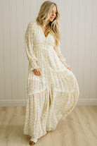 Woman wearing a long, light-colored floral dress against a white paneled wall.