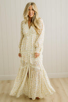 Woman wearing a long floral dress standing against a white paneled wall.
