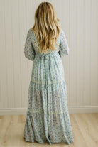 Woman wearing a floral dress standing against a white paneled wall.