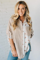 Woman wearing a layered outfit with a striped shirt over a floral top against a white brick wall.