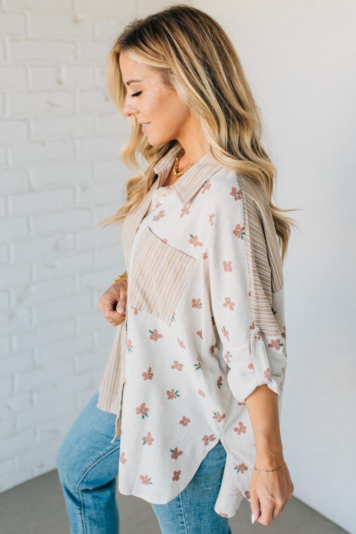 Woman wearing a floral blouse with fringe details against a white brick wall.