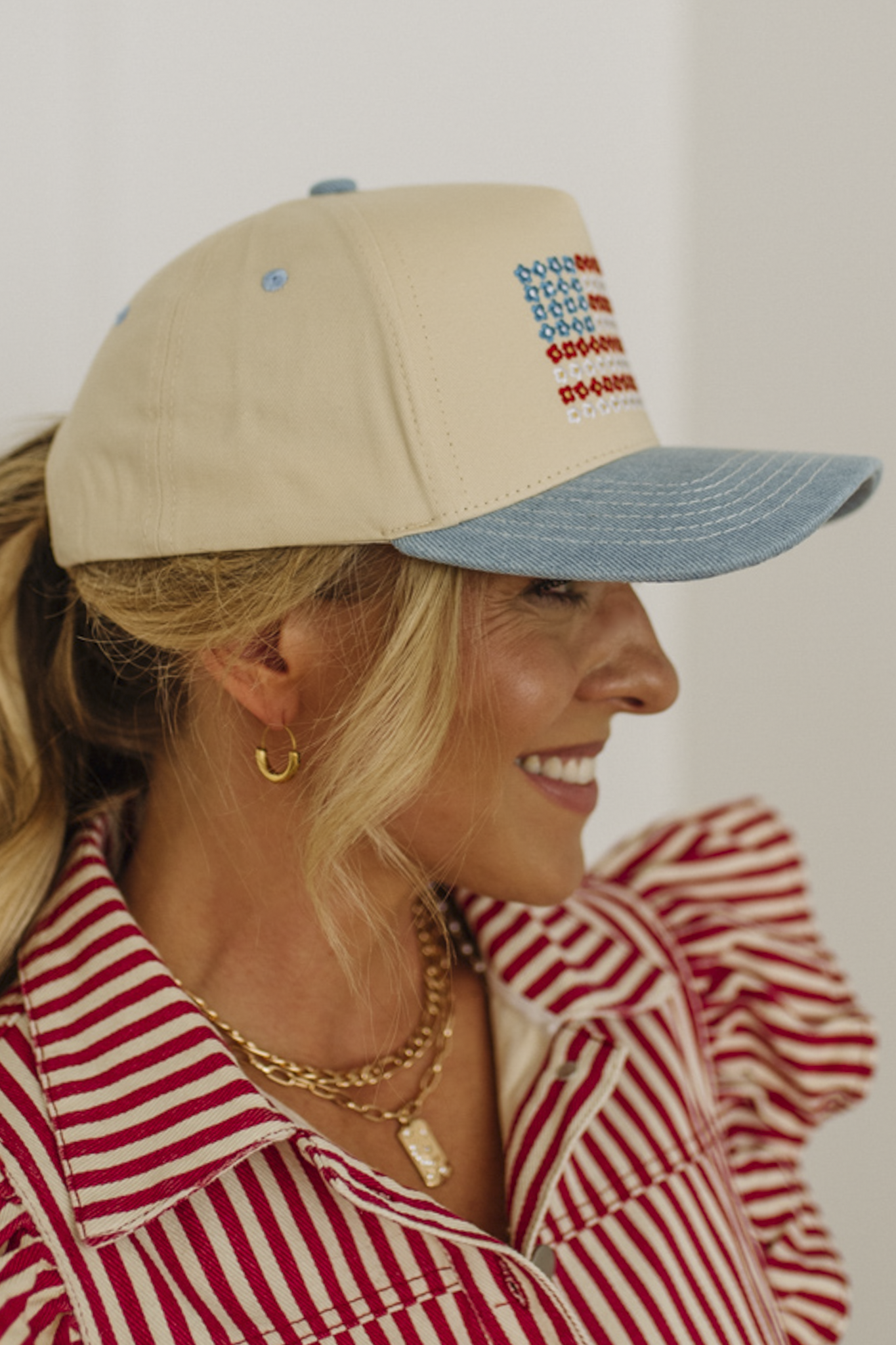 Woman wearing a beige and blue cap with embroidered text, smiling against a white background
