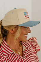 Woman wearing a beige and blue cap with embroidered text, smiling against a white background