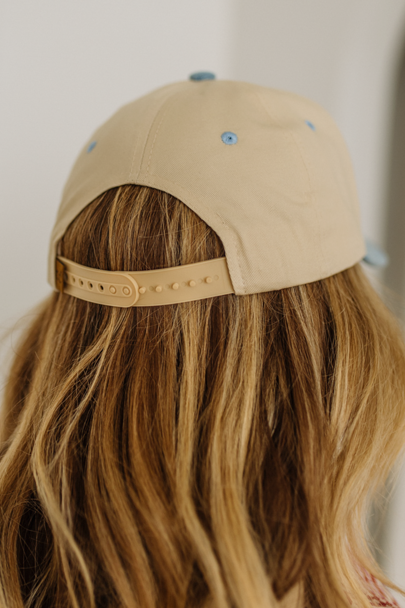 Beige cap worn by a person with long blonde hair against a neutral background