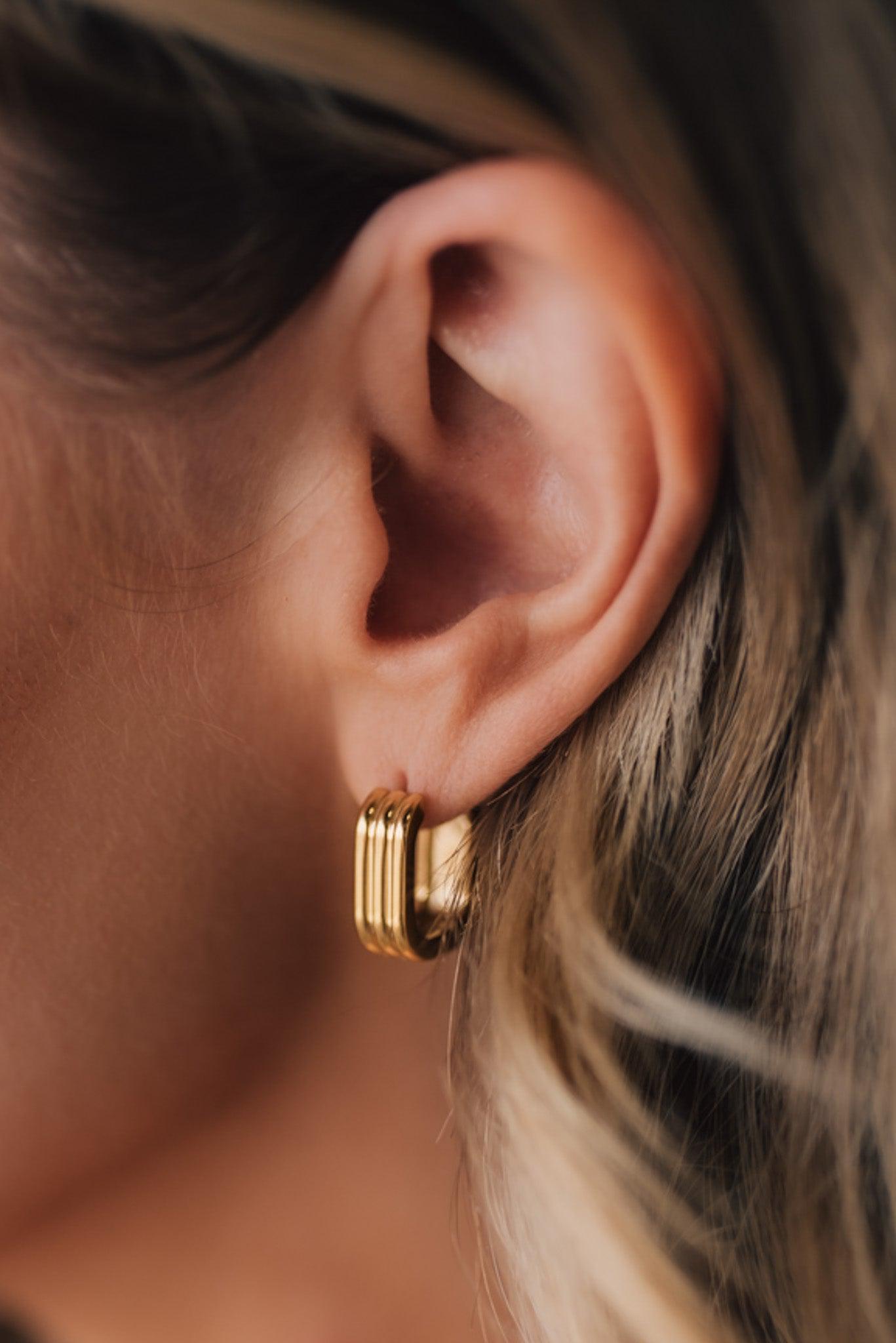 Woman modeling gold huggie earrings featuring a 3 row stacked detail