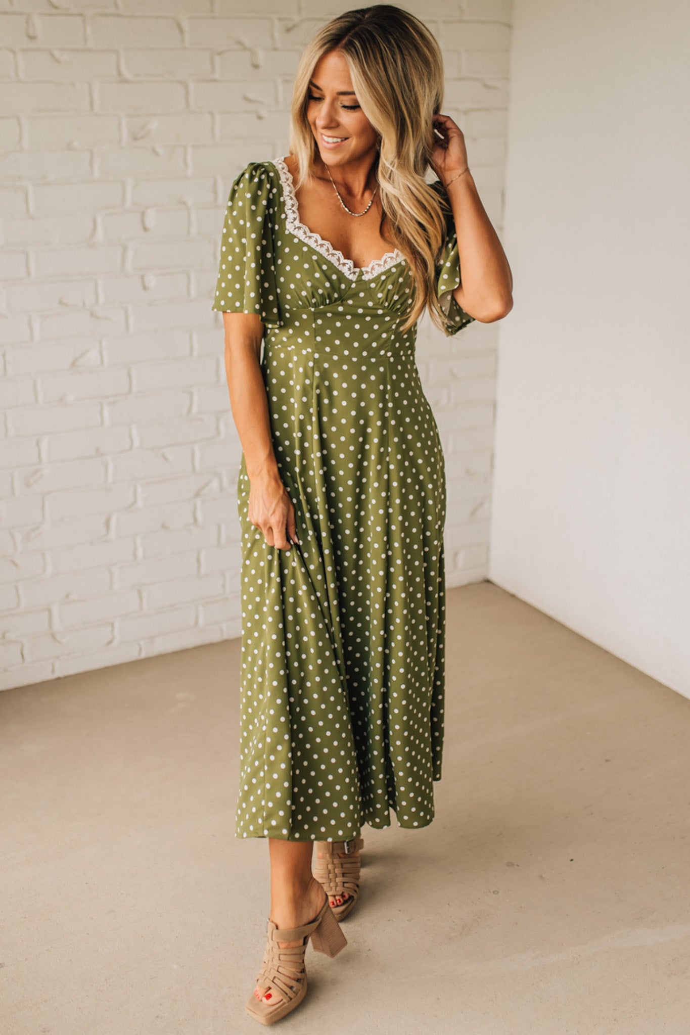 Woman wearing a green polka dot dress against a white brick wall.