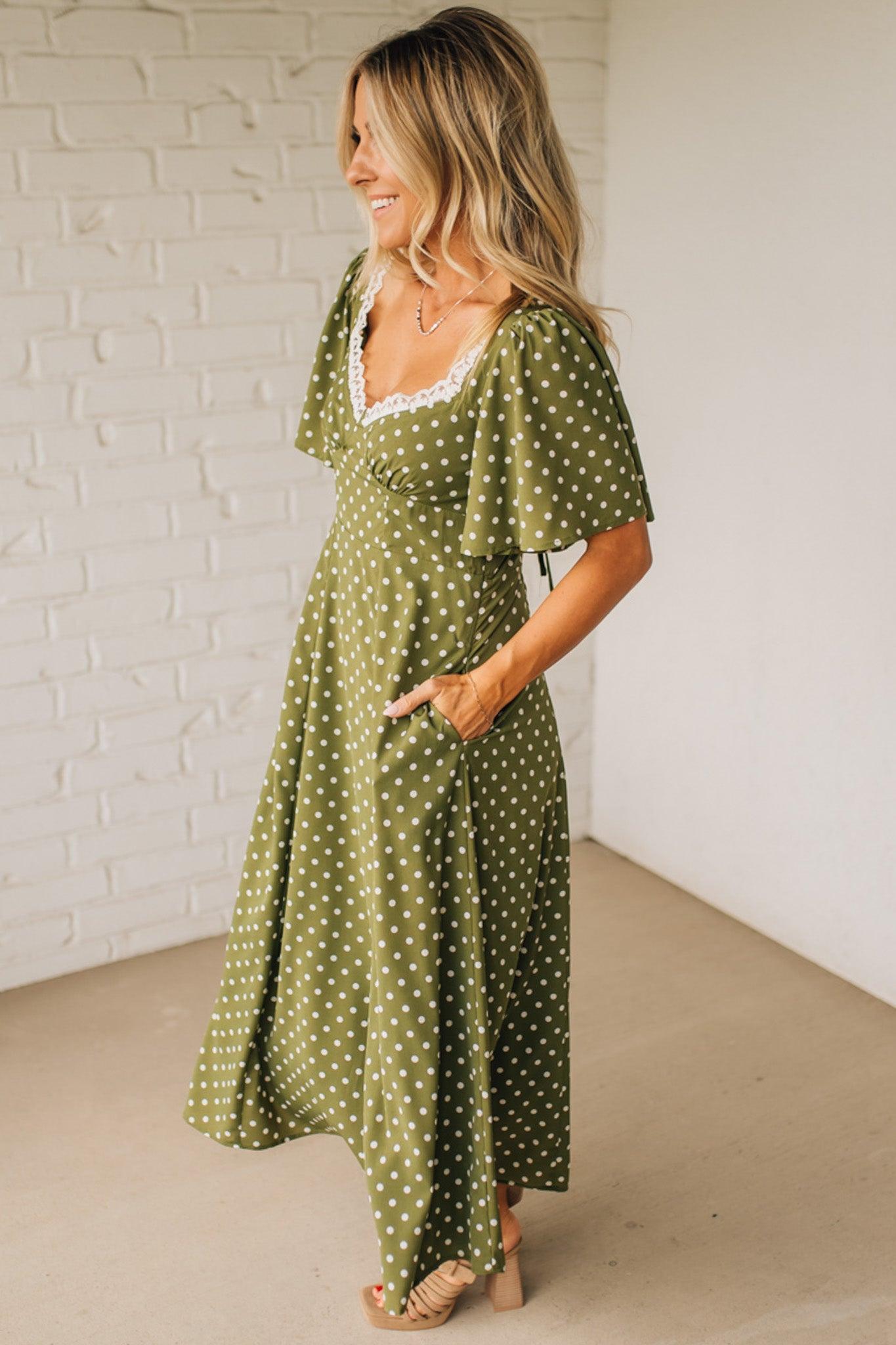Woman wearing a green polka dot dress against a white brick wall.