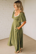 Woman wearing a green polka dot dress against a white brick wall.