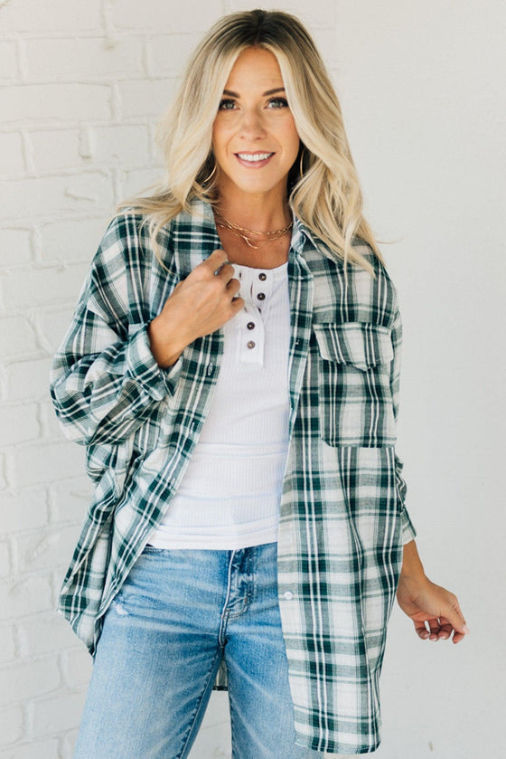 Woman wearing an oversized plaid top in dark green and ivory tones.