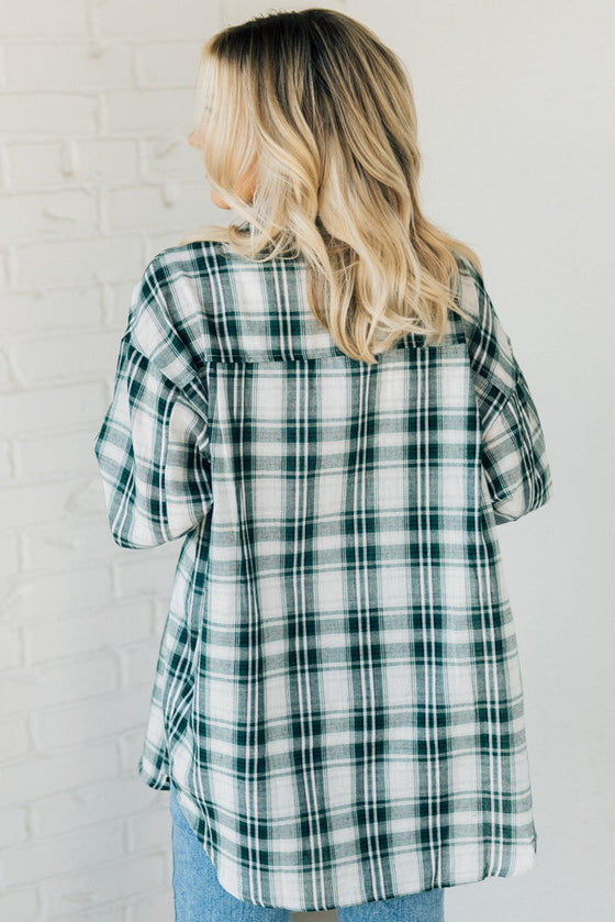 Woman wearing an oversized plaid top in dark green and ivory tones.