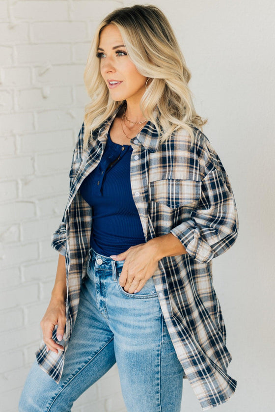 Woman wearing an oversized plaid top in navy, cream and brown tones.