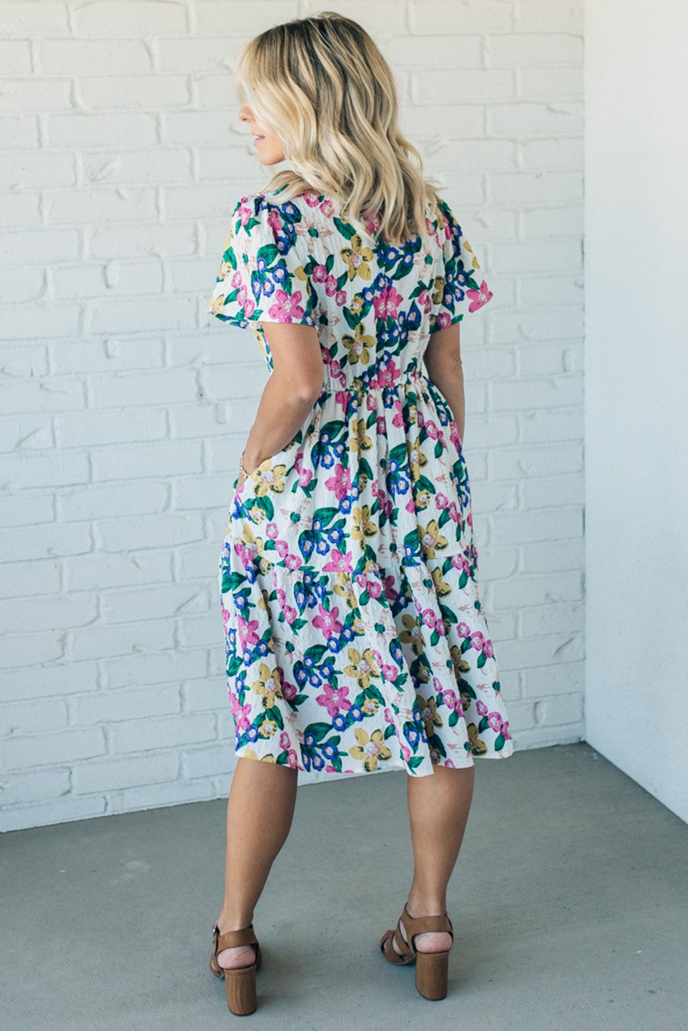 Women wearing a short sleeve midi dress that is Ivory with purple, pink and yellow flowers throughout.
