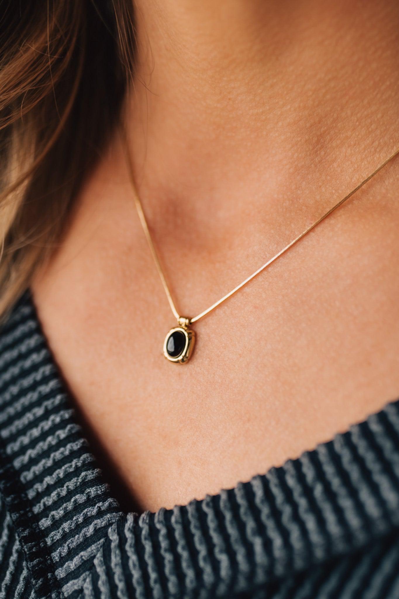 black stone necklace with gold trim and gold chain modeled with a v neck top