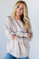 Woman wearing a beige oversized sweater with blue jeans against a white background