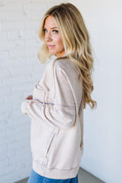 Woman wearing a beige jacket against a white brick wall