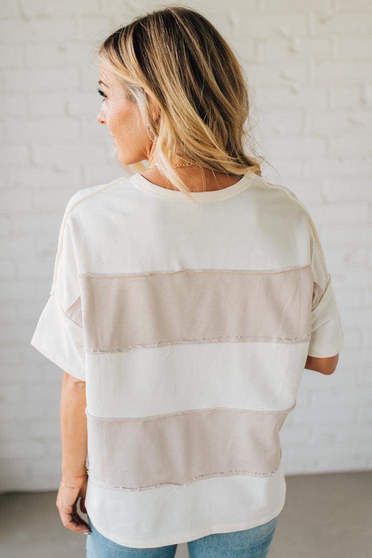 Woman wearing a white and beige striped shirt against a plain background