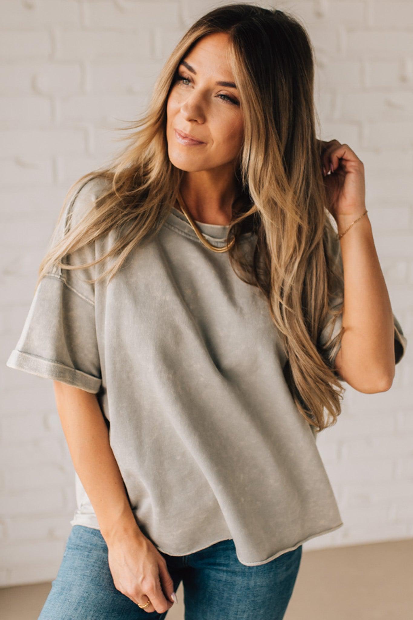 BLONDE WOMAN WEARING A FRENCH TERRY, ACID-WASHED TEE SHIRT WITH RAW EDGE ON NECKLINE AND A BOXY FIT.