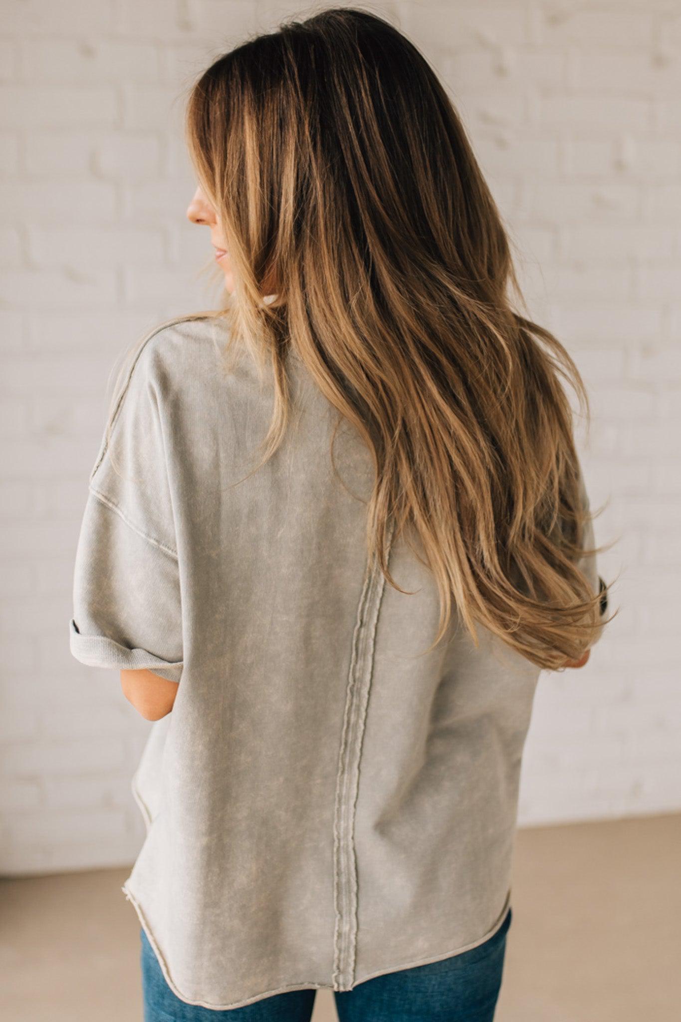 BLONDE WOMAN WEARING A FRENCH TERRY, ACID-WASHED TEE SHIRT WITH RAW EDGE ON NECKLINE AND A BOXY FIT.