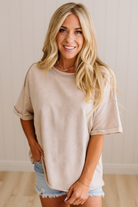 Woman wearing a beige oversized t-shirt and denim shorts indoors.
