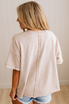 Person wearing a beige seam back top with denim shorts against a neutral background