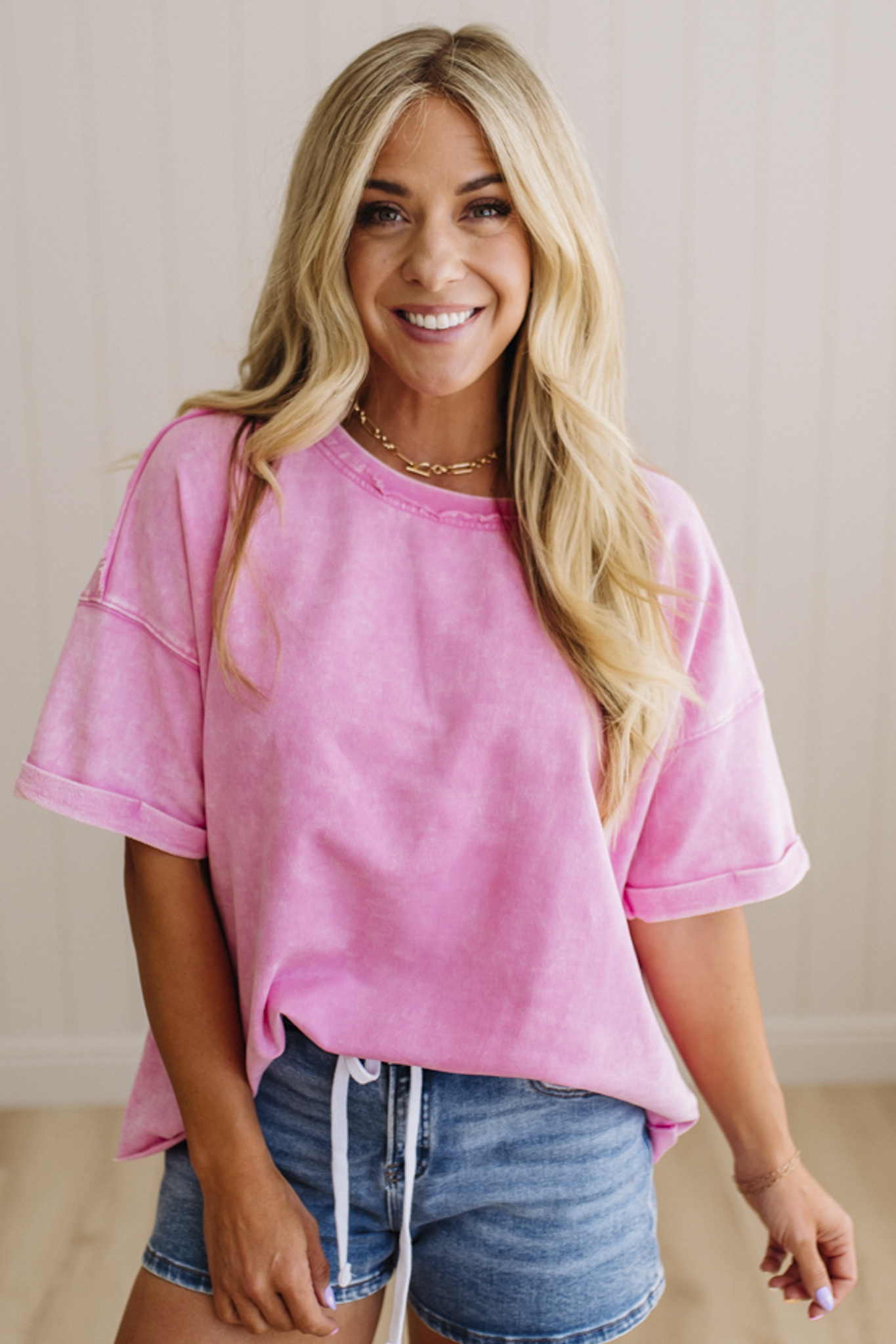 Woman wearing a pink oversized t-shirt and denim shorts indoors.