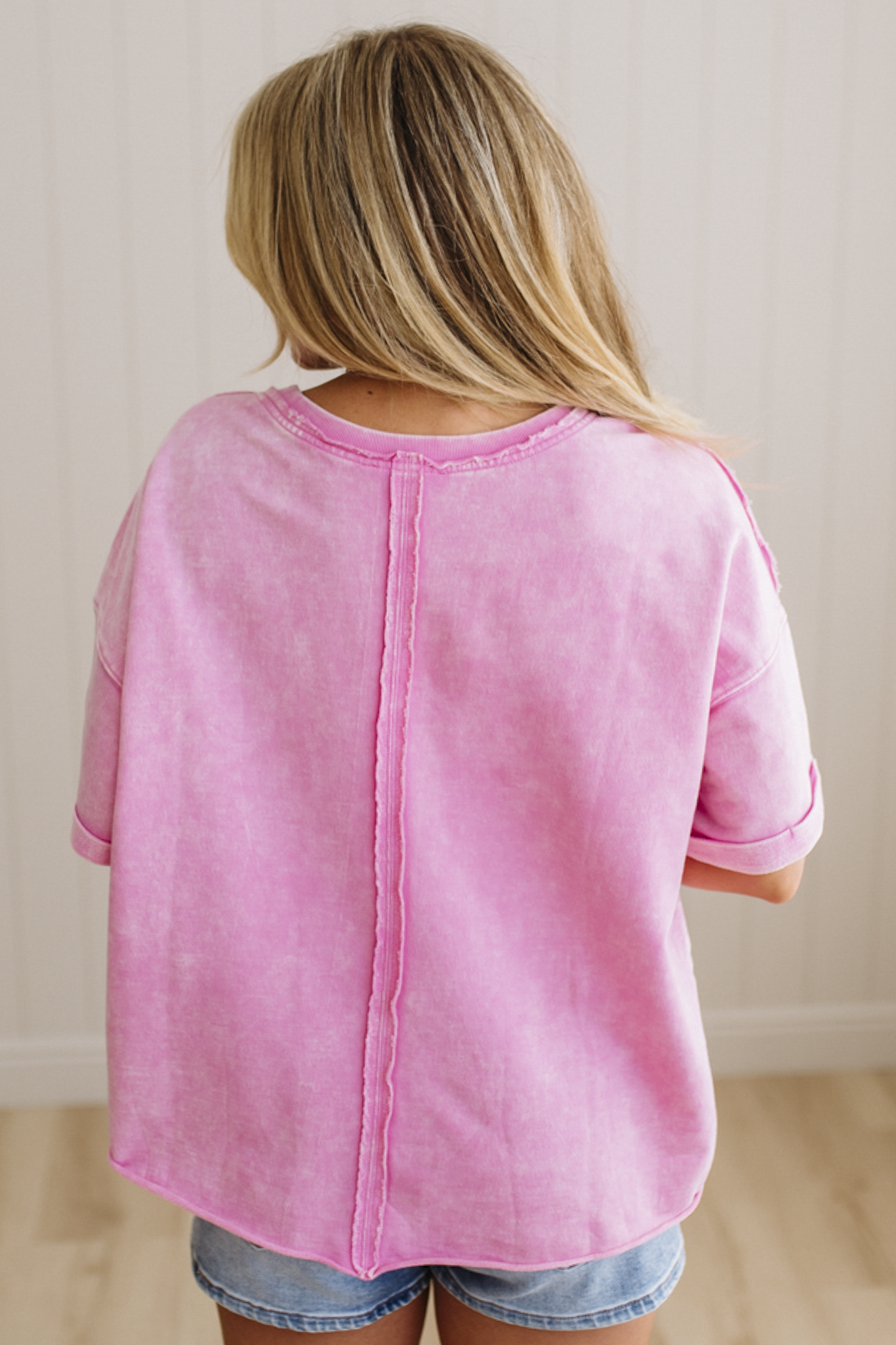 Person wearing a pink shirt and denim shorts against a plain background