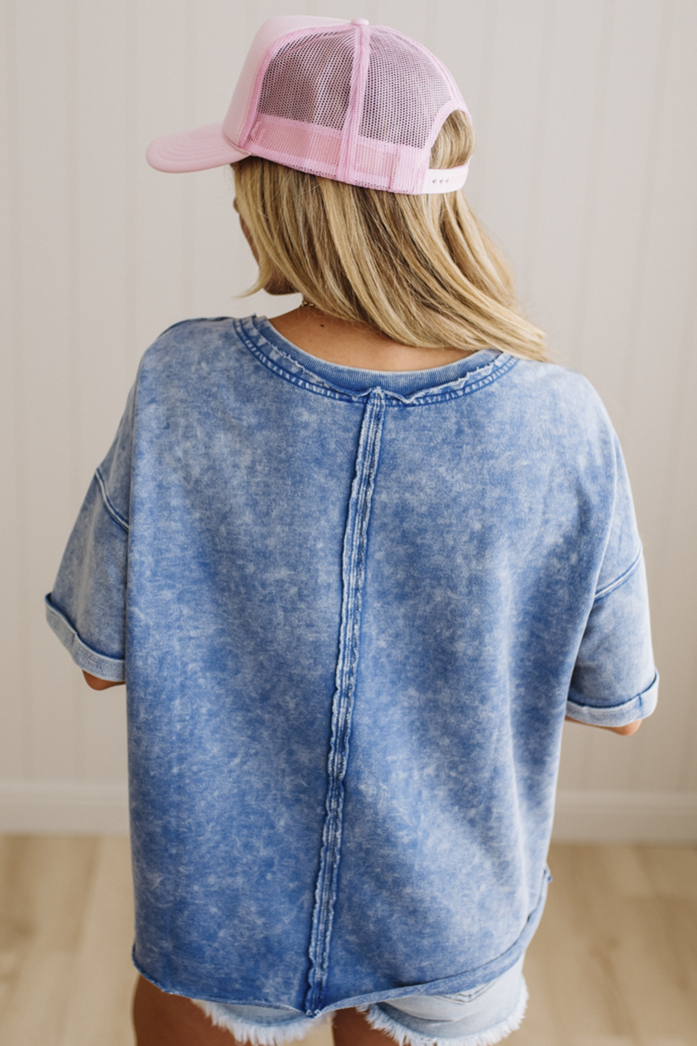 Person wearing a blue acid-wash shirt and pink cap from behind